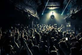 Interior del club con multitud de personas bailando bajo luces de neón y un disco de discoteca