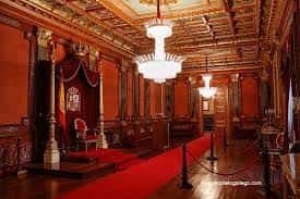 Sala principal del palacio con alfombra roja, cortinajes y lámparas de cristal