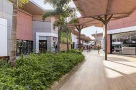 Paseo exterior del centro comercial con vegetación y estructura de sombra moderna
