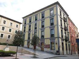 Fachada principal del edificio amarillo en la plaza, con detalles arquitectónicos y árboles jóvenes