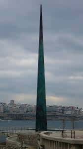 Vista frontal del Obelisco Millennium en A Coruña con cielo nublado y ciudad al fondo