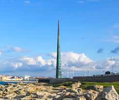 Obelisco Millennium desde la costa con cielo azul y formaciones rocosas en primer plano