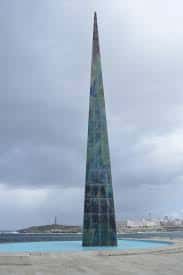 Obelisco Millennium rodeado de agua y con vista al faro y la ciudad al fondo