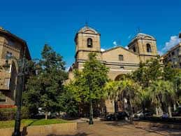 Exterior de la iglesia rodeada de árboles y plaza pública, mostrando su entorno urbano