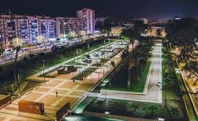 Vista nocturna del parque iluminado con edificios urbanos al fondo