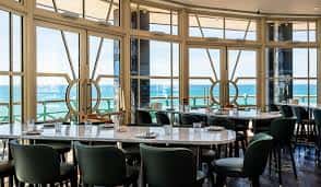 Interior del restaurante con mesas dispuestas para eventos y grandes ventanales con vista al océano