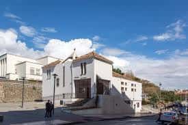 Exterior de la parroquia con personas caminando y cielo parcialmente nublado