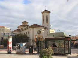 Vista general de la parroquia desde la plaza con parada de autobús y entorno urbano