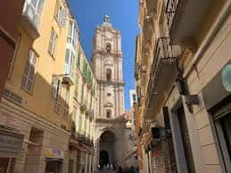 Vista exterior de la torre de la Iglesia de San Juan Bautista desde una calle estrecha de Málaga