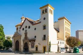 Vista exterior de la Parroquia de San Pedro Apóstol en Málaga con su fachada blanca y torre campanario bajo un cielo azul
