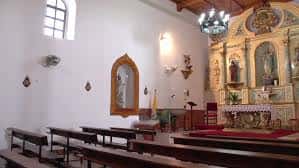 Capilla lateral de la parroquia con retablo dorado, bancos de madera y iluminación natural por ventana alta