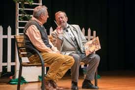 Escena de una obra de teatro con dos actores sentados en un banco en el escenario