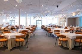 Salón de banquetes preparado con mesas cuadradas y sillas naranjas