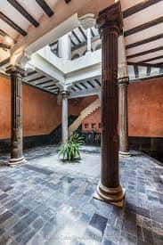 Patio interior con columnas, escalera y planta decorativa bajo luz natural