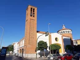 Vista exterior de la Parroquia de San José Obrero y San Francisco de Paula en Sevilla, destacando su torre de ladrillo y fachada moderna bajo cielo azul