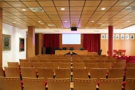 Aula magna con butacas dispuestas en gradas y pantalla de proyección frontal