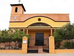 Entrada frontal de la iglesia con portón negro, columnas laterales y vegetación alrededor, ideal para eventos al aire libre