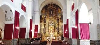 Interior de la iglesia con altar mayor dorado y cortinajes rojos en las columnas