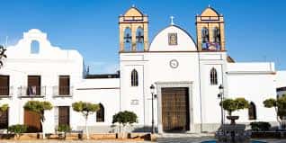Vista exterior de la capilla con torres campanario y jardines frontales