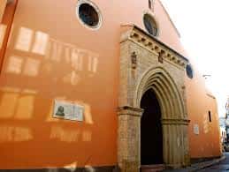 Fachada lateral de la Capilla de San Andrés con arco de entrada gótico y pared naranja
