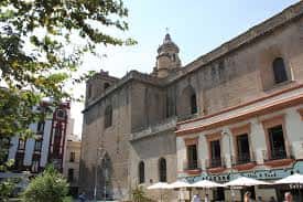 Fachada lateral de la Iglesia de la Anunciación con árboles y terrazas de cafetería en primer plano