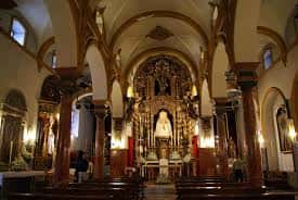 Vista del presbiterio y altar principal con iluminación cálida y detalles arquitectónicos barrocos