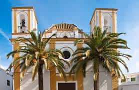 Vista frontal de la iglesia con palmeras y torres gemelas bajo el sol