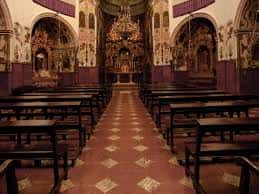 Interior de la capilla con banco de madera, altar dorado y decoración religiosa