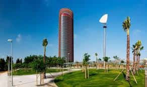 Paisaje urbano del parque con palmeras, césped y la Torre Sevilla como referencia arquitectónica