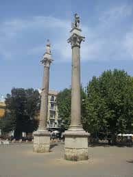 Detalle de las columnas de la Alameda de Hércules con vegetación y edificios al fondo