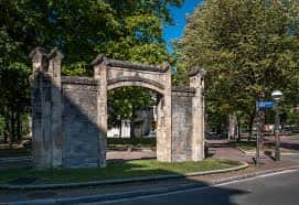 Puerta del Asilo de San Cristóbal en Vitoria, estructura histórica de piedra con arco central y columnas flanqueadas por árboles