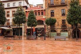Vista general de la Plaza de Riego en Oviedo con edificios históricos y árboles en un día lluvioso
