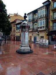 Monumento central en la Plaza de Riego rodeado de arquitectura tradicional asturiana