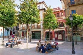 Plaza de Riego con personas descansando en bancos bajo la sombra de árboles en un día soleado