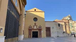 Entrada lateral de la iglesia con puerta de madera y ventana circular en fachada amarilla