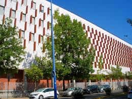 Entrada principal de la Facultad de Comunicación con vehículos estacionados y cielo despejado