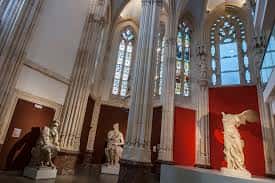Interior del museo con columnas altas, vitrales y estatuas en exhibición
