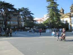 Vista diurna de la plaza con personas caminando y árboles frondosos