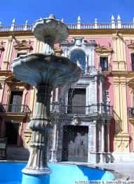 Detalle de la fuente barroca en primer plano con la fachada del palacio al fondo