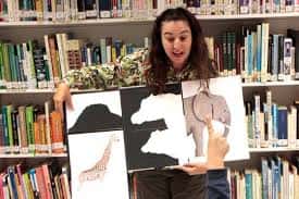 Actividad de cuentacuentos en la biblioteca con una mujer mostrando ilustraciones de animales frente a estanterías de libros