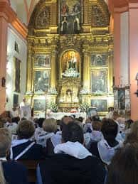 Vista interior de la iglesia durante una celebración religiosa con el retablo al fondo