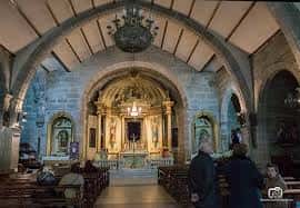 Interior de la iglesia con altar barroco, bóvedas de piedra y fieles en oración