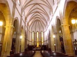 Interior de la iglesia con bóvedas de crucería, columnas de piedra y altar iluminado por luz natural