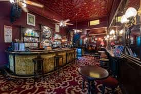 Interior del bar con barra de madera, alfombra roja y iluminación cálida