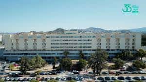 Fachada principal del hospital con estacionamiento y montañas al fondo