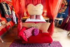 Habitación temática con decoración roja vibrante, cama con dosel y mobiliario bohemio