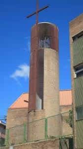 Torre de la parroquia con cruz en la parte superior y cielo azul de fondo