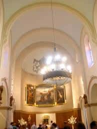 Interior de la iglesia con altar, cuadro central y lámpara colgante durante una ceremonia