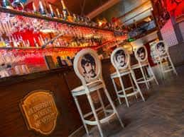 Interior del bar con estantería de botellas y taburetes decorados con retratos