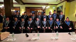 Grupo de personas en traje formal con medallas, posiblemente en un acto institucional o ceremonia dentro de un salón elegante
